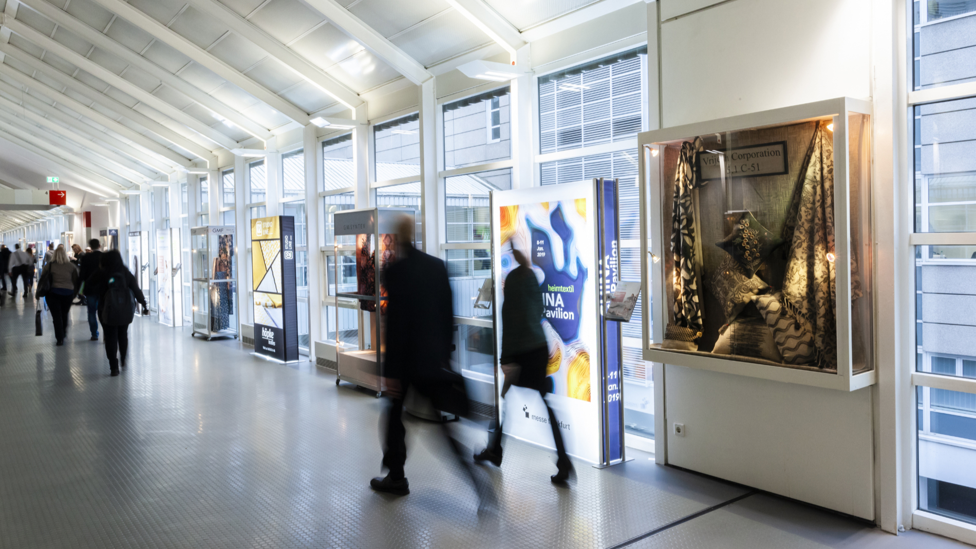 Besucher laufen an einer Vitrine auf dem Messegelände vorbei